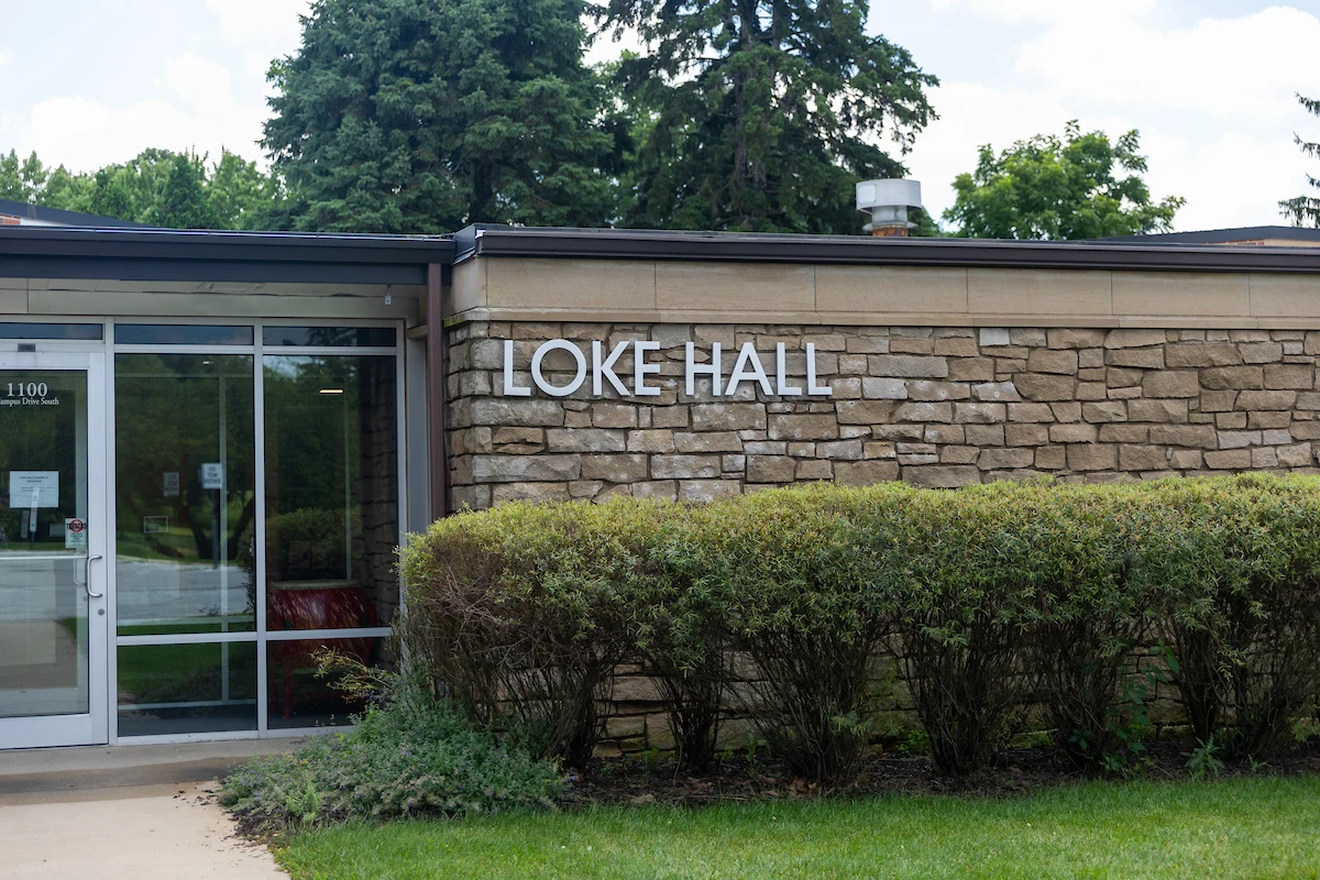 Exterior of Loke Hall, a building with stone walls, bushes, and glass entrance doors, home to valuable Multicultural Resources for students.