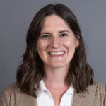 Smiling woman with wavy brown hair wearing a plaid blazer and white shirt on a gray background, featuring Bethany Garling-Spychala.