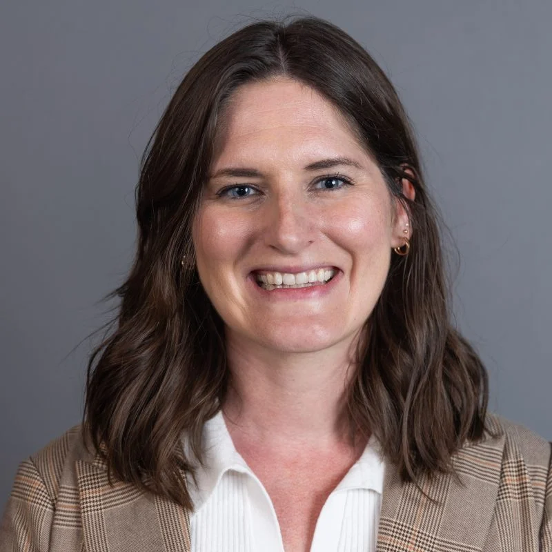 Smiling woman with wavy brown hair wearing a plaid blazer and white shirt on a gray background, featuring Bethany Garling-Spychala.
