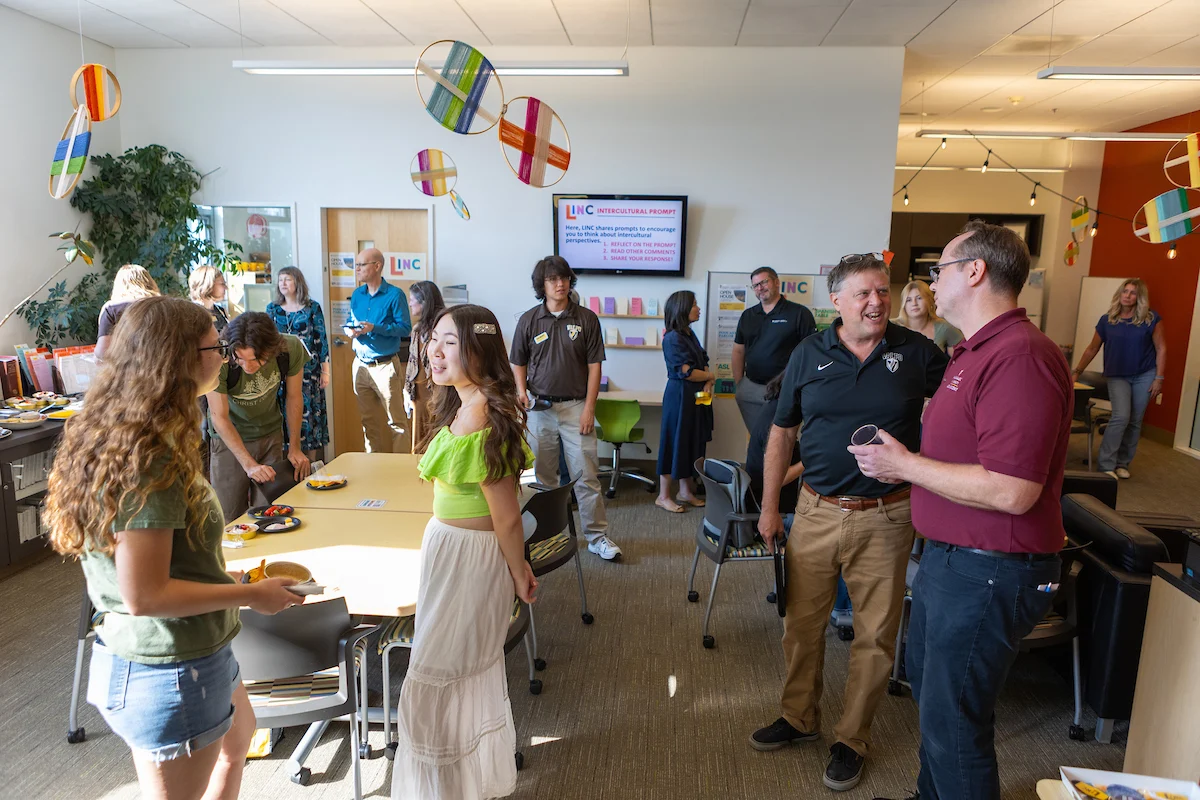 People talking and mingling at a casual indoor social event with snacks, colorful hanging decorations, and lively discussions about study abroad experiences.