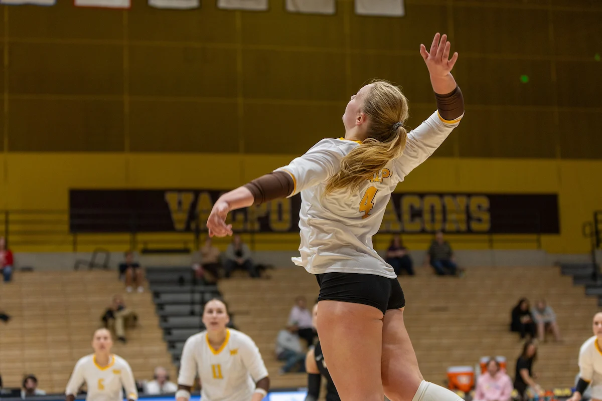 A volleyball player jumps to spike the ball during a game in a gymnasium, showcasing teamwork and strategy—skills essential in Marketing and Communications.