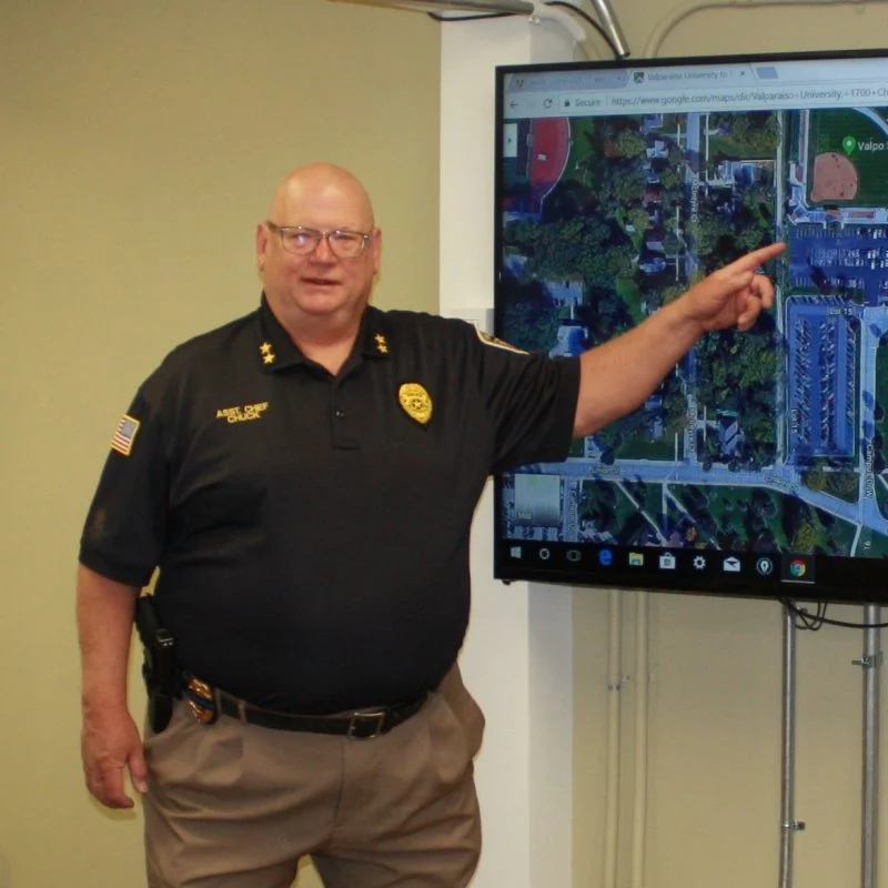 Bald man in police uniform, identified as Charles P. Garber Jr, points at a map on a large screen mounted on the wall.