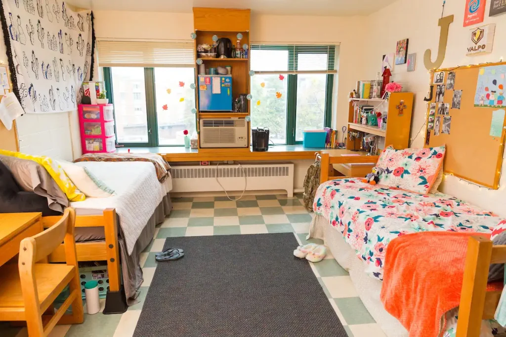 A bright college dorm room with two beds, desks, shelves, and large windows in the background—ideal for students seeking Off-Campus Housings with comfortable study and living spaces.