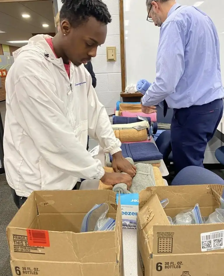 A person practices CPR compressions on a manikin while another stands nearby at a training table, learning life-saving skills through WAVES training.