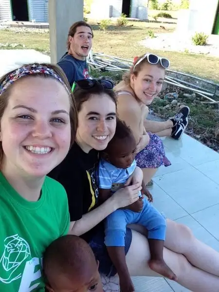 Four young adults sit outside on a sunny day, smiling as two small children giggle on their laps and WAVES of laughter fill the air.