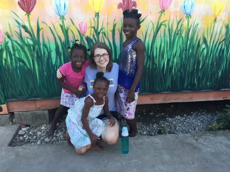 Four smiling girls pose together in front of a colorful mural painted with vibrant flowers and WAVES on a wall.