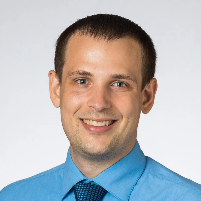 Smiling man in a light blue dress shirt and tie against a plain, light background—Jesse Sestito, Ph.D.