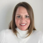 Jamie Stangel, Ph.D., with straight brown hair and a white turtleneck, smiles in front of a plain light background.