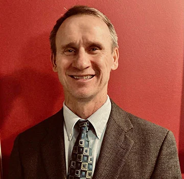 Smiling man in a suit and tie, identified as Jeffrey Emmons, standing in front of a red wall.