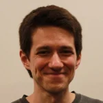 Jesse Curtis, a man with short brown hair, smiles in front of a plain light-colored background.