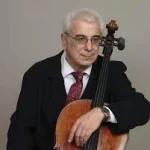 David Machavariani, an elderly man in a suit, holds a cello while seated against a plain background.