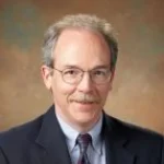 A middle-aged man with glasses, gray hair, and a mustache, identified as Richard E. DeMaris, Ph.D., wearing a suit and tie, smiling slightly.