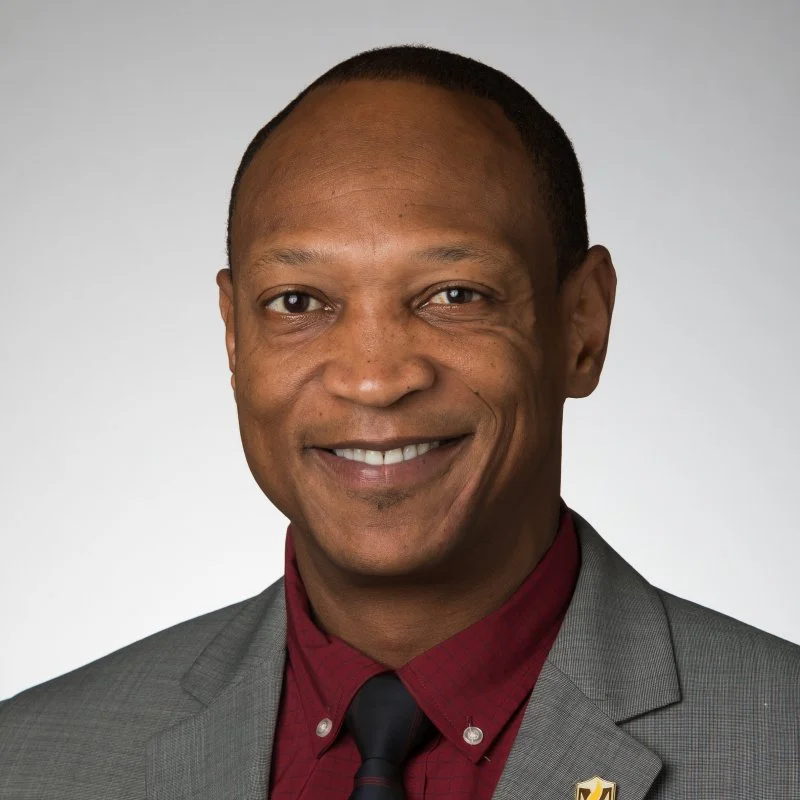 Smiling man, Richard Sévère, in a gray suit and red shirt against a plain light background.