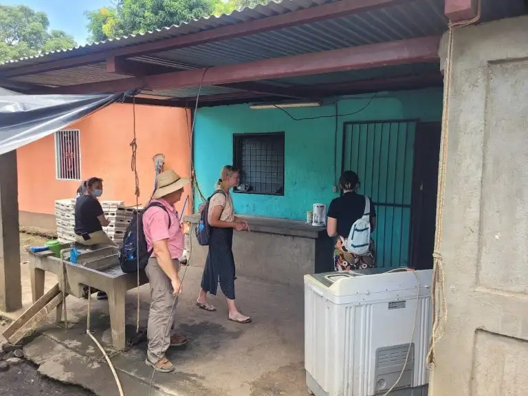 Four people stand outside a blue building with WAVES painted on the side, one at a counter and others waiting behind.