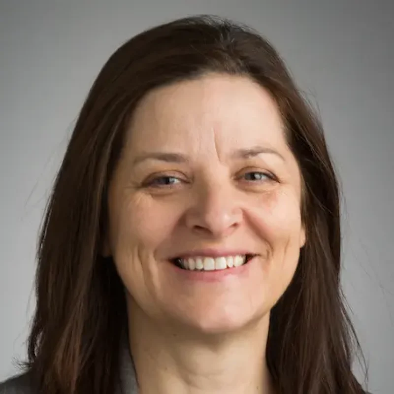 Smiling woman, Sedefka Beck, Ph.D., with straight brown hair against a plain, light gray background.