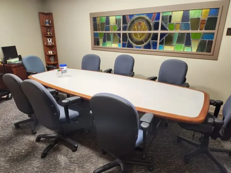 A conference room in Loke Hall with eight chairs around a table and a stained glass artwork on the wall.