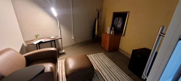 Cozy office in Loke Hall with an armchair, floor lamp, rug, small table, coat rack, and cabinet against a yellow wall.