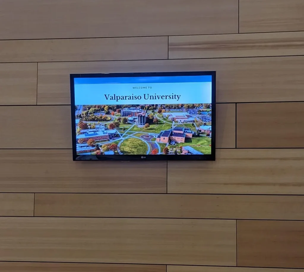 A wall-mounted screen in Harre Union displays "Welcome to Valparaiso University" above a campus aerial photo.