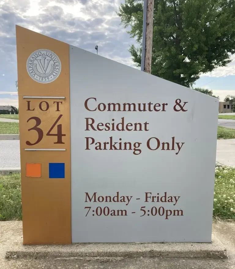 A parking sign reads "LOT 34 Commuter & Resident Parking Only, Mon-Fri, 7:00am-5:00pm," situated near a road and grassy area.