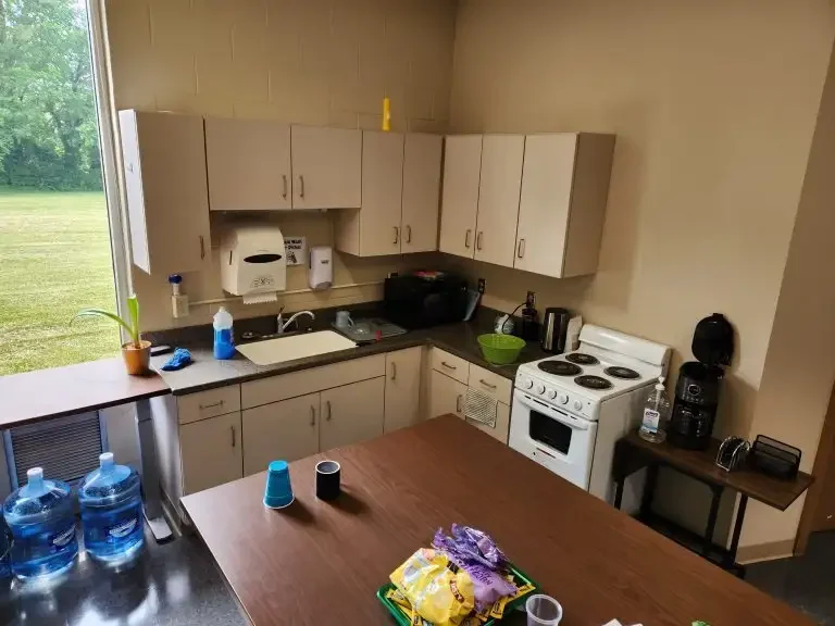 Small office kitchen in Loke Hall with cabinets, sink, stove, coffee maker, and snacks on the counter, all situated near a window.