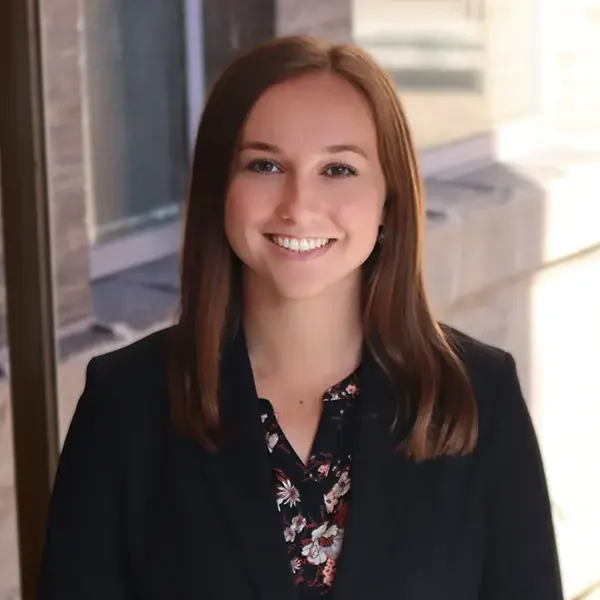 A woman with straight brown hair in a black blazer smiles in a bright indoor setting, representing the accomplished alumni of Valparaiso University.
