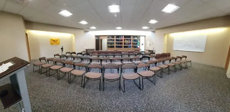 Conference room in Loke Hall with rows of empty chairs facing a whiteboard and shelves at the front.