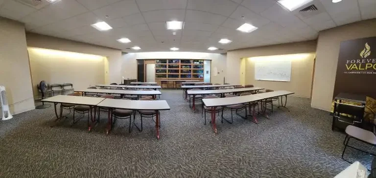 Empty Loke Hall classroom with U-shaped tables, chairs, whiteboard, and "Forever Valpo" sign on the right wall.