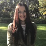 Lisa Doering, a woman with long dark hair, smiles outdoors in a park with trees and grass in the background.