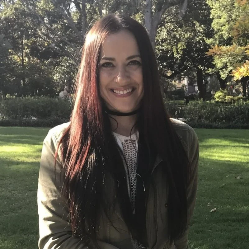 Lisa Doering, a woman with long dark hair, smiles outdoors in a park with trees and grass in the background.