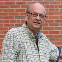 Ronald Janke, Ph.D., an older man in glasses and a plaid shirt, stands in front of a brick wall, looking at the camera.