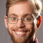 A smiling man with glasses, light brown hair, and a beard, facing the camera—Jeffrey Pruet.
