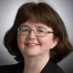 Jennifer Holt, a woman with short brown hair, glasses, and a black blazer, smiles at the camera.