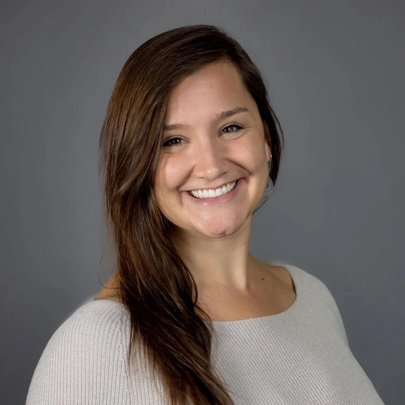 Katie Zromkoski, OTD, a woman with long brown hair smiling and wearing a light gray top, stands against a plain gray background.